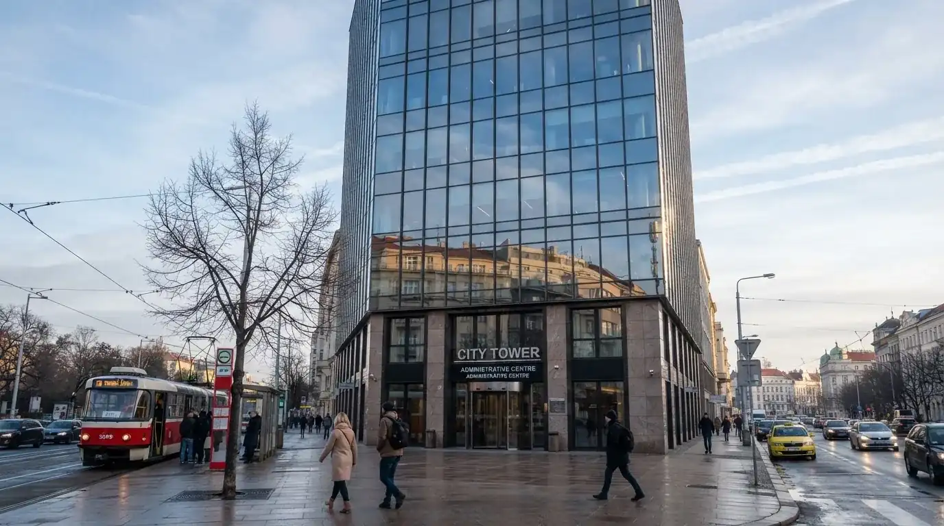 Fasáda moderní administrativní budovy s skleněnými okny odráží ranní oblohu nad rušnou pražskou ulicí.